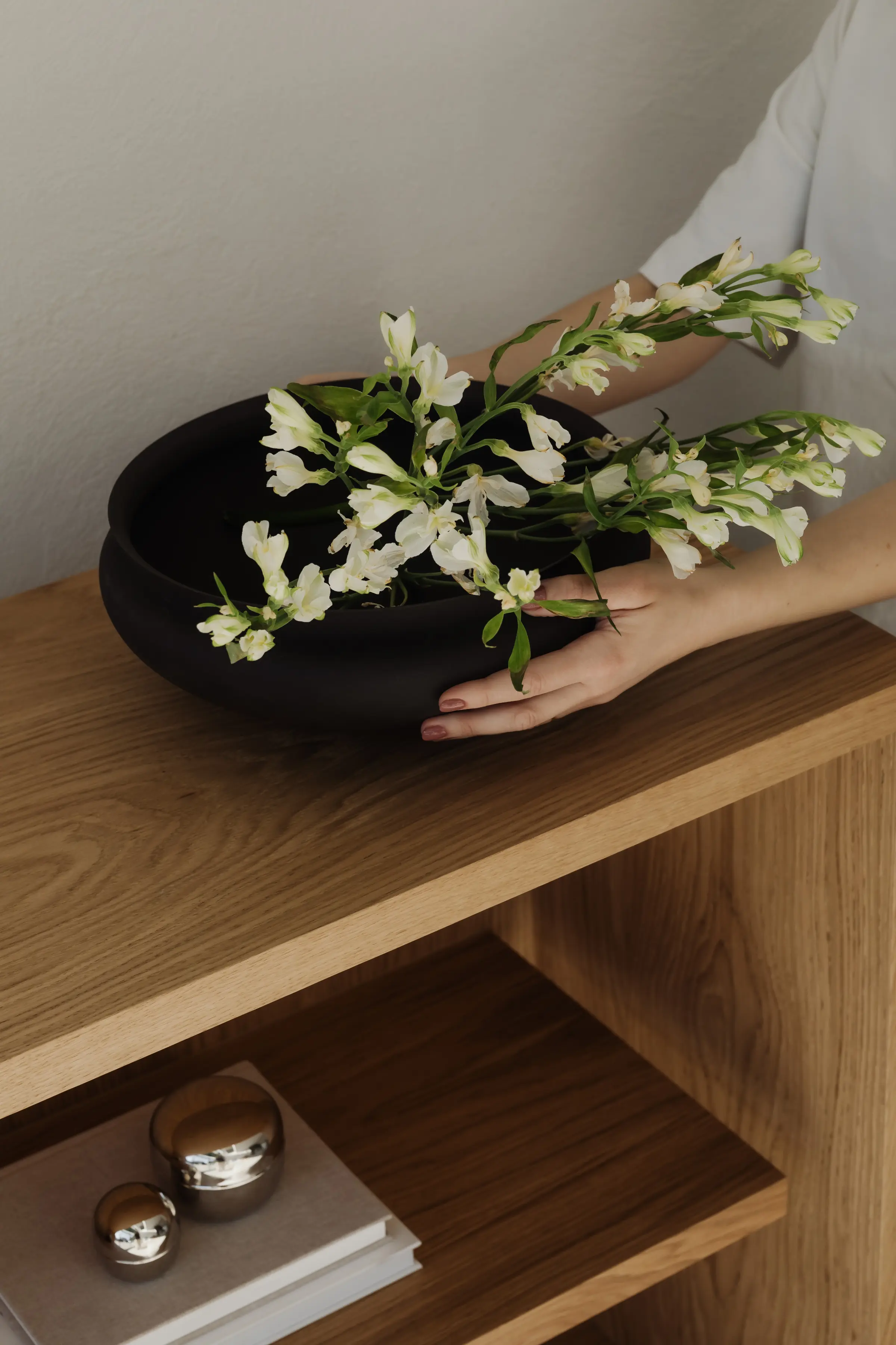 Woman arranging white flowers in black bowl